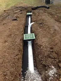 A partially buried white drainage pipe is surrounded by soil.